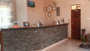 A reception area with a stone counter, clocks, a TV, and a 'Wash Room' sign. - Samanene Beach Hotel (Mwanza)