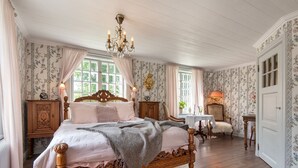 Une chambre spacieuse avec un grand lit, une tête de lit en bois sculptée et un lustre.