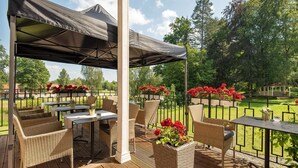 Une terrasse extérieure aménagée avec des meubles en osier, des tables et un espace couvert offrant une vue sur un terrain de golf.