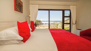 A hotel room with a large bed, a red and white bedspread, and a view of the beach through a large window. - ArchRock Resort (Keurboomstrand)