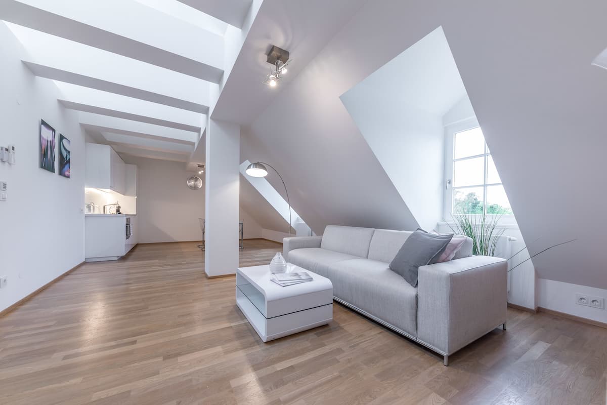 A modern loft with a high ceiling, a dining area, and a living space with a sofa and ottoman.