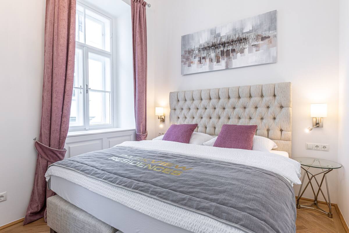 A neatly arranged bedroom with a large bed, a glass side table, and a wall-mounted artwork.