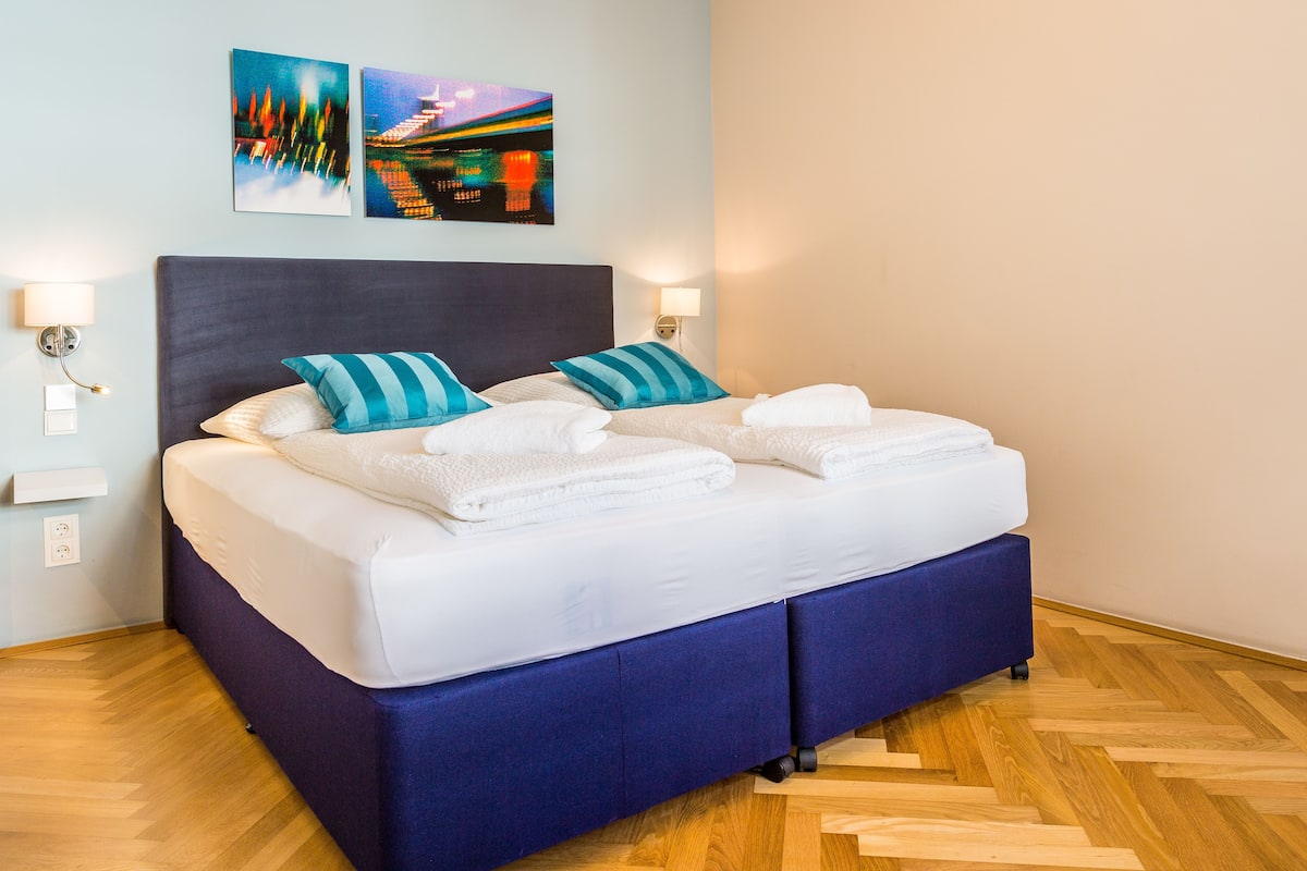 A neatly made bed with white linens and two blue-striped pillows, a dark headboard, and two wall-mounted lights.