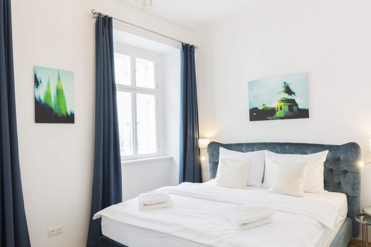 A bedroom with a large bed, a chandelier, and two paintings on the walls.