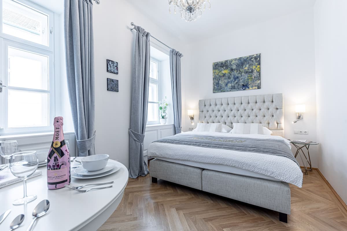A modern bedroom with a large bed, a bedside table, a chandelier, and a window with curtains.