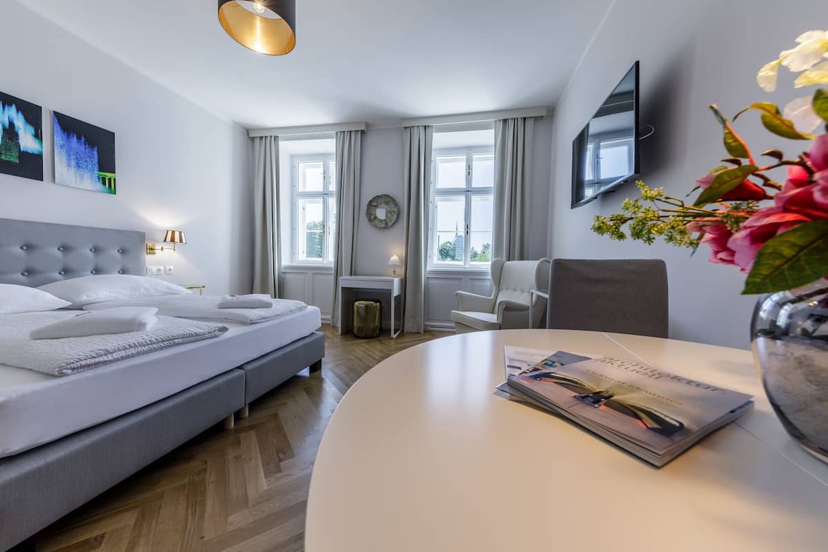 A modern hotel room with a bed, a desk, a chair, a TV, and a window with curtains.