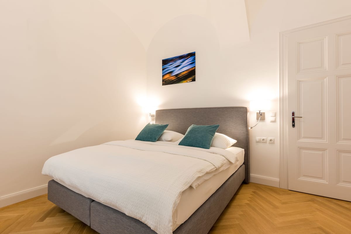 A bedroom with a bed, two pillows, a painting on the wall, and a door.