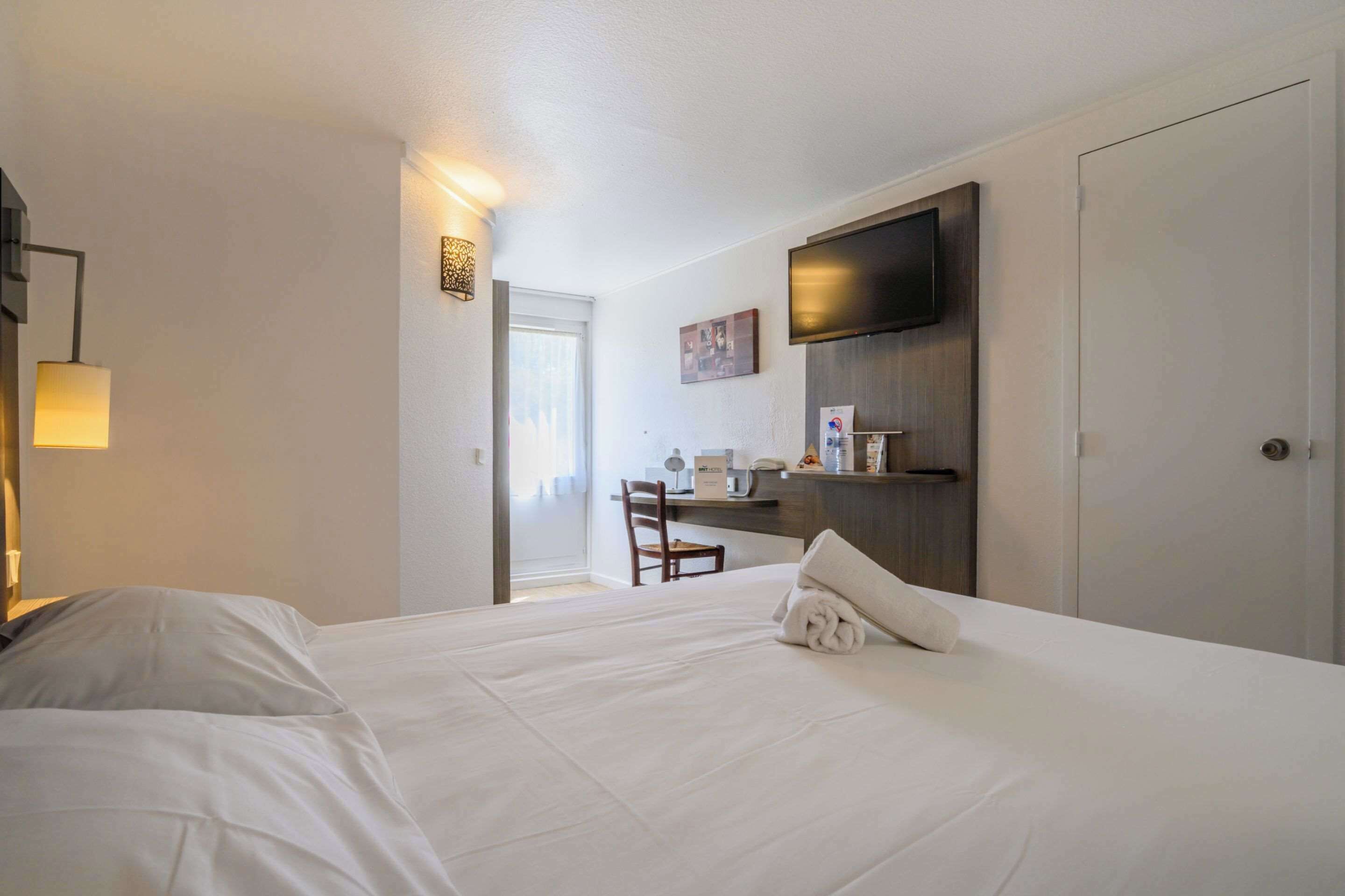 A hotel room with a bed, a desk, a chair, a TV, and a wardrobe.