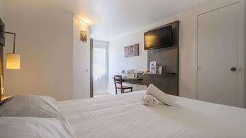 A hotel room with a bed, a desk, a chair, a TV, and a wardrobe.