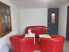 A room with a red sofa, two red chairs, a white table, and a door marked "la 20".