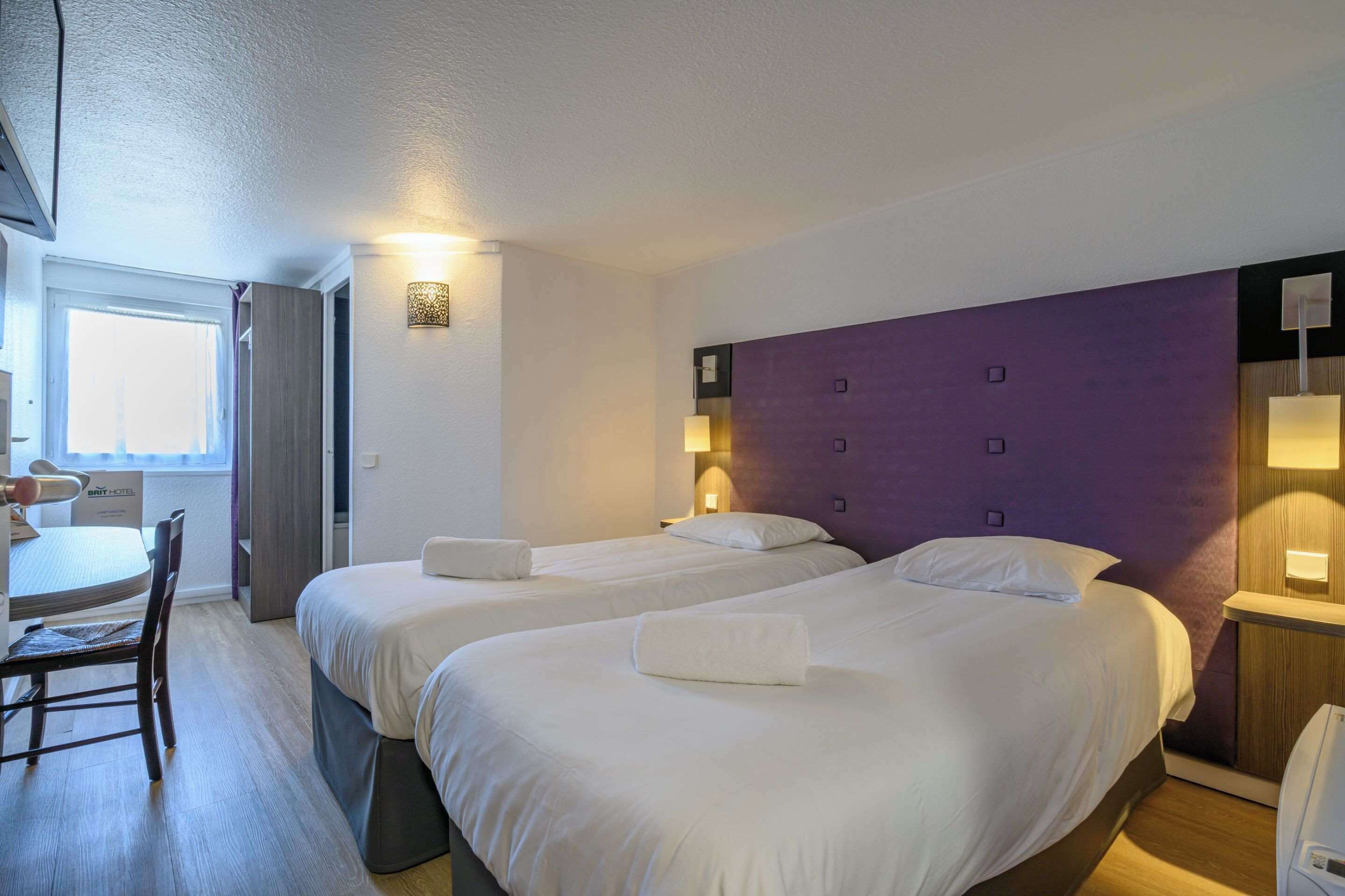 A hotel room with two beds, a desk, and a chair.
