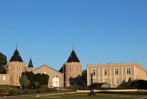 A large building with three towers and a symmetrical facade, surrounded by a well-maintained garden.
