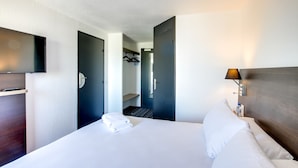 A hotel room with a bed, a nightstand, a lamp, and a wardrobe. - Brit Hotel Reims la Neuvillette (Reims)