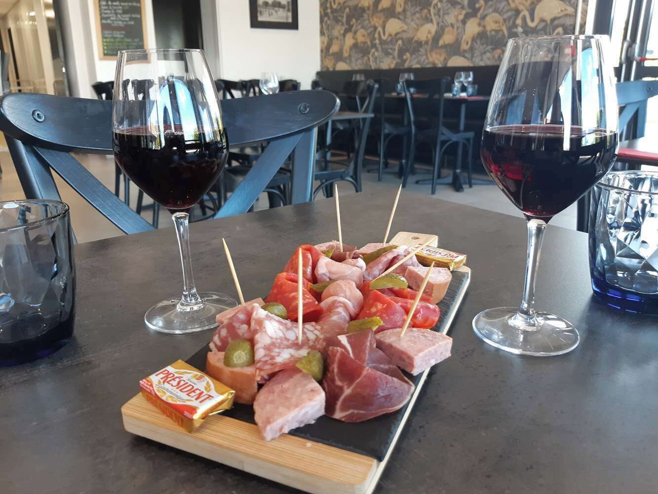 A table with a charcuterie board, two glasses of red wine, and a menu board in the background.