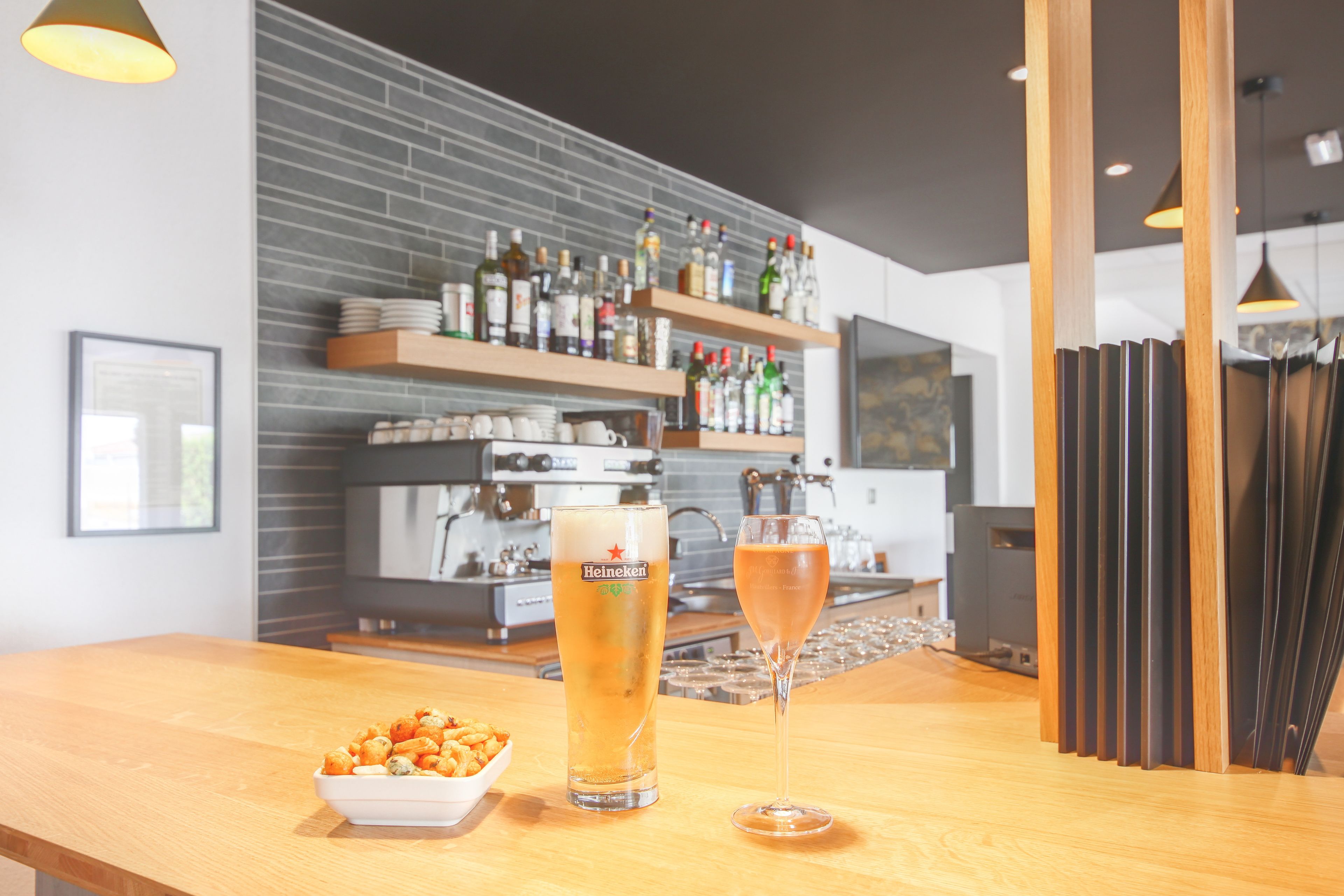 Un coin bar avec un verre à bière et un verre à vin posés sur le comptoir, un bol de collations et, en arrière-plan, un mur de briques orné d’étagères remplies de bouteilles.