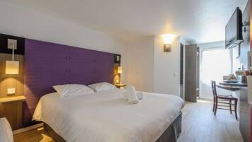 A hotel room with a large bed, a desk with a chair, a television, and a window with curtains.