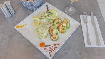 Plat blanc amb peix a la planxa, rodanxes de llimona i un tomàquet petit, acompanyat d'un got de vi blanc i un cistell de pa.