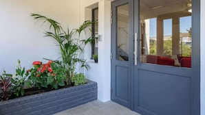 A modern building entrance with a grey door, a small window, and a planter with various plants. - Brit Hotel Reims la Neuvillette (Reims)