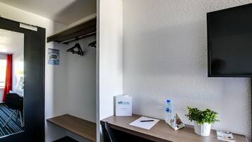 A hotel room with a wooden desk, a flat-screen TV mounted on the wall, a small potted plant, a water bottle, and a BRIT HOTEL sign.