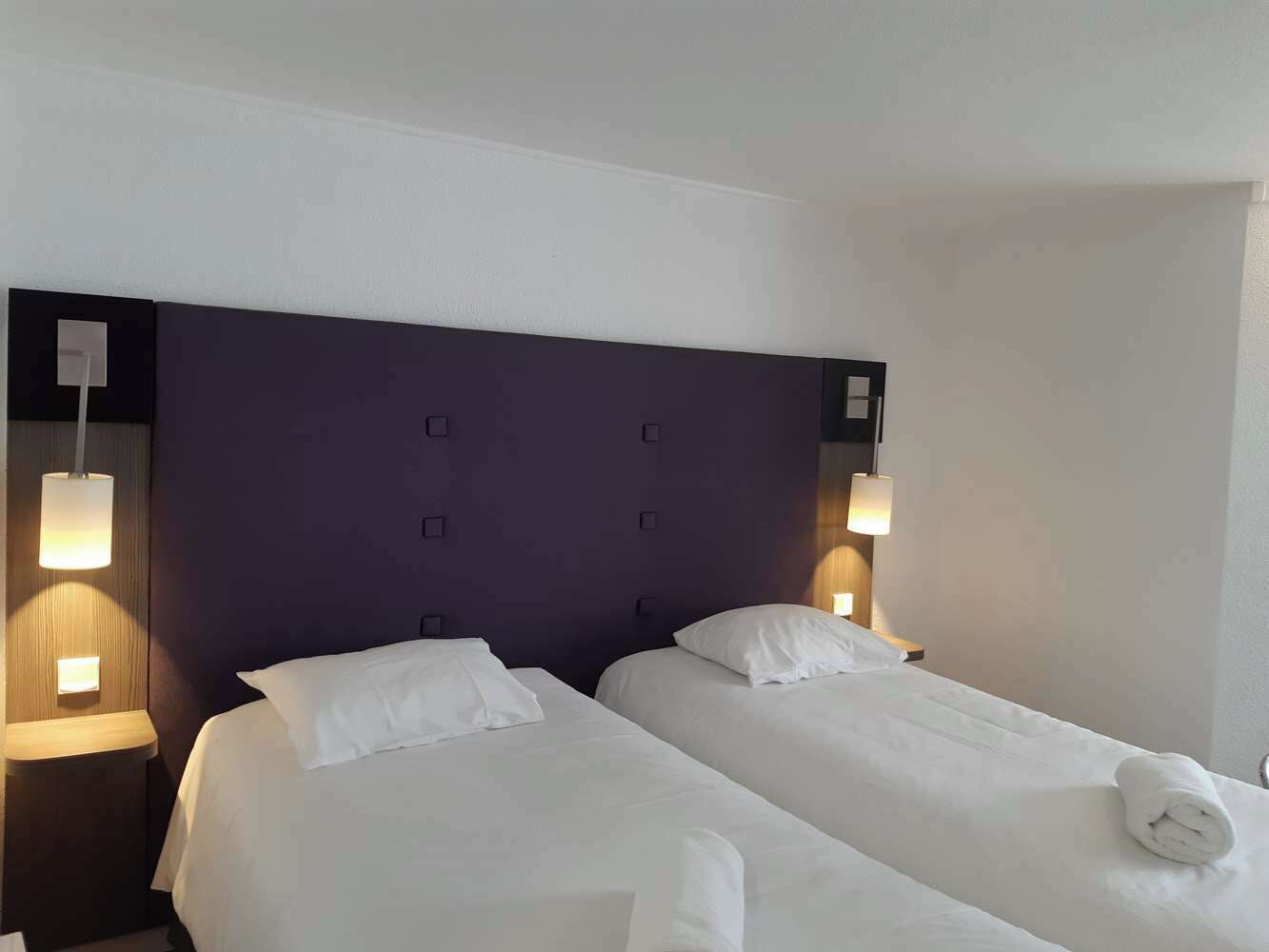 Una habitación de hotel con dos camas individuales, un cabecero oscuro y lámparas de noche.