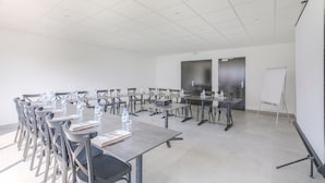 A conference room with multiple tables and chairs, equipped with water bottles and papers, and a whiteboard. - Brit Hotel Reims la Neuvillette (Reims)