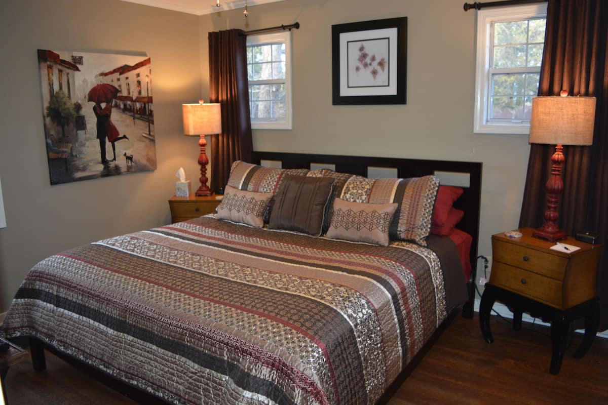 A neatly made bed with a patterned bedspread, a bedside table with a lamp, and a framed picture on the wall.