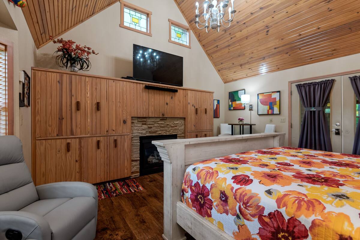 A bedroom with a large bed, wooden walls, a television, a fireplace, and a chandelier.