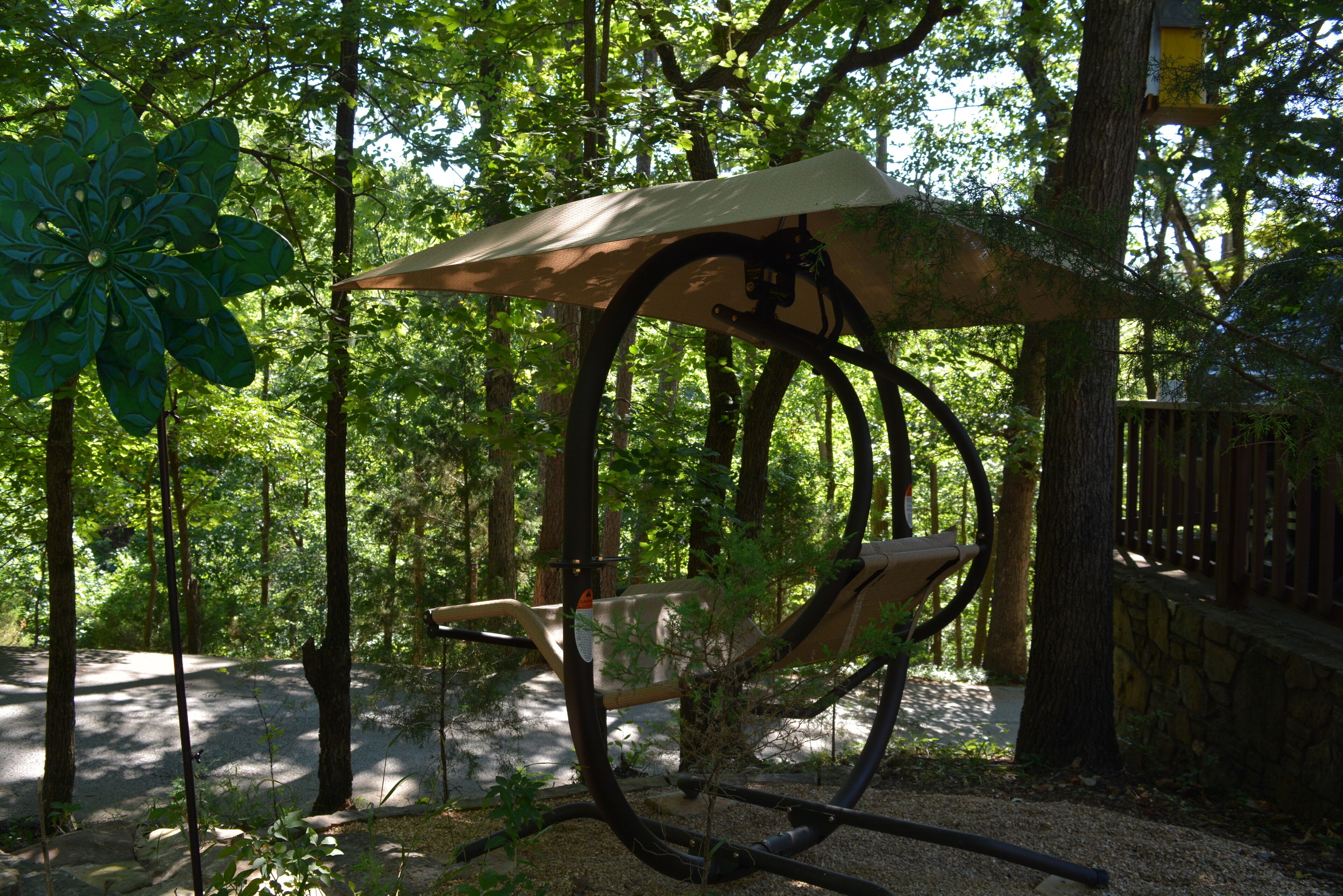 A hammock chair in a wooded area with a stone wall and wooden fence.