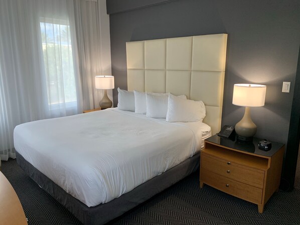 A hotel room with a large bed, two bedside tables with lamps, a nightstand, and a carpeted floor.