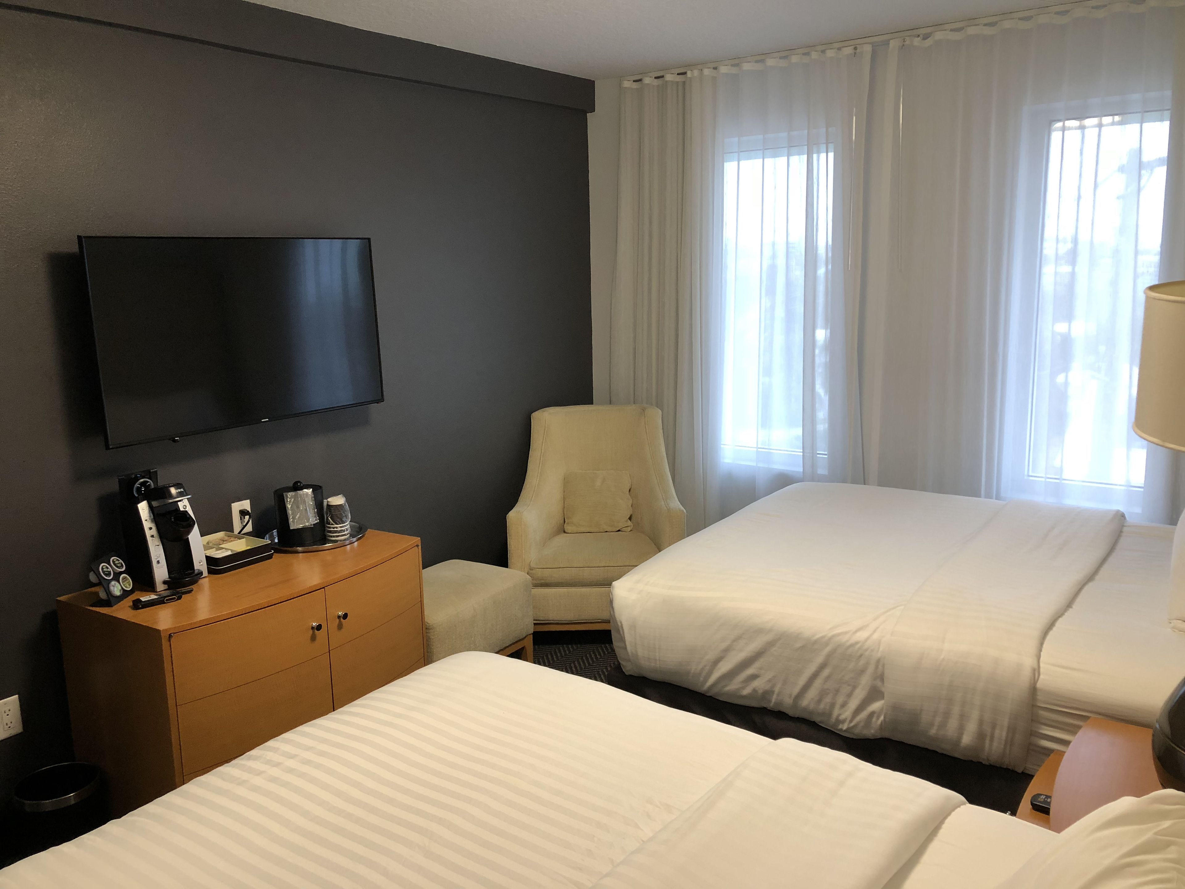 A hotel room with two beds, a TV, a coffee maker, and a chair.