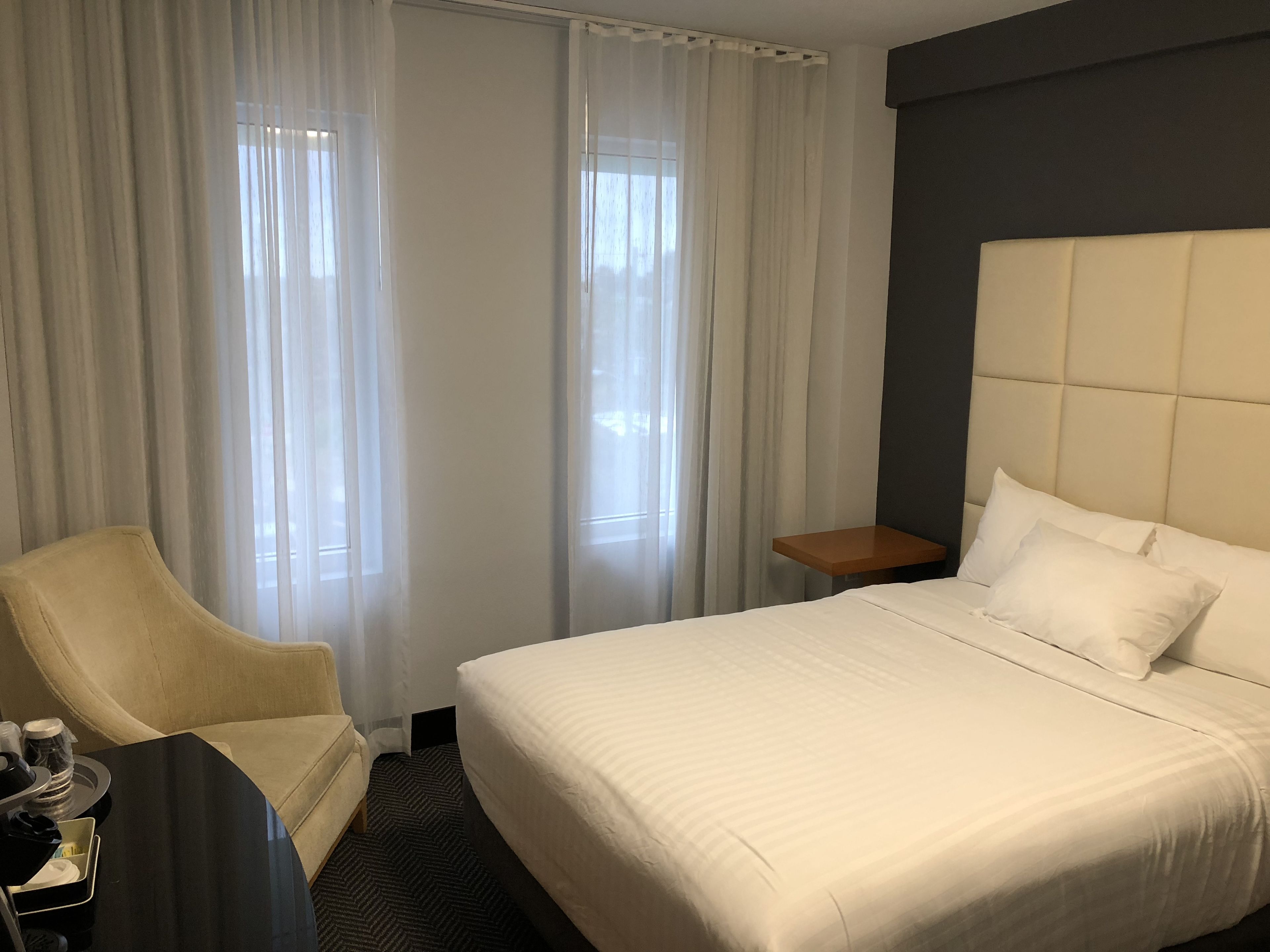Een hotelkamer met een bed, een stoel, een klein tafeltje en gordijnen.
