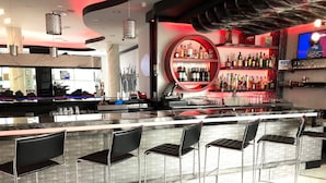 Un espace bar moderne doté d’un comptoir en marbre, de tabourets de bar noirs rembourrés et d’une étagère circulaire où sont exposées différentes bouteilles.