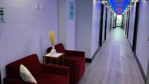 Un couloir d’hôtel avec des sièges rouges, une petite table sur laquelle est posé un vase, et des panneaux de signalisation fixés aux murs.