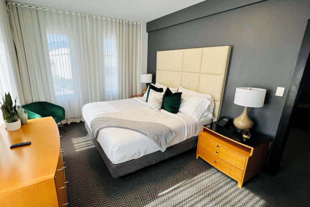 A hotel room with a large bed, a desk, a chair, a lamp, and a TV.