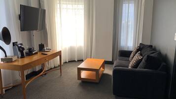 A hotel room with a wooden desk, a television, a sofa, and a coffee machine.