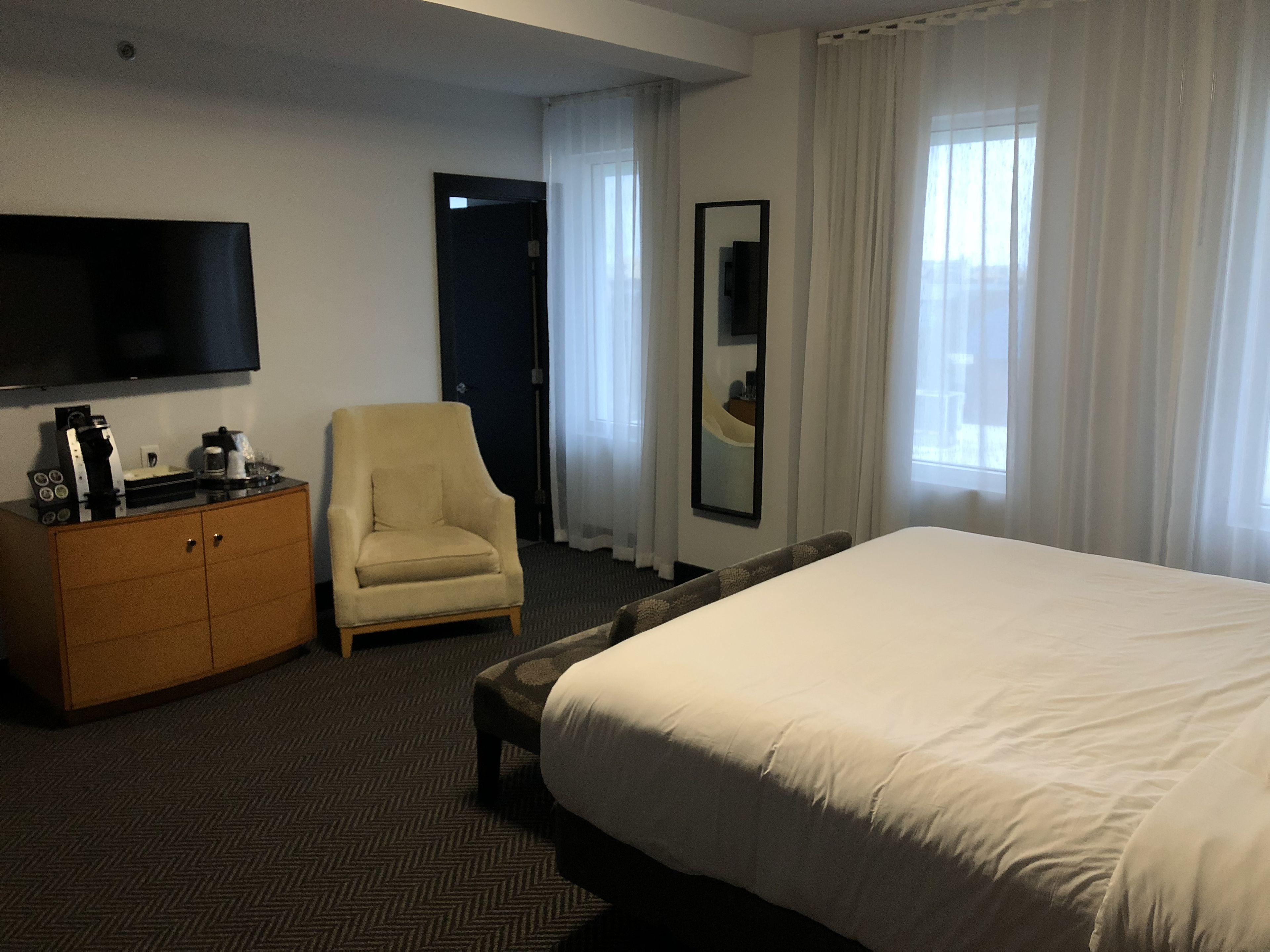 A hotel room with a large bed, a wooden dresser, a chair, a flat-screen TV, and a mirror.