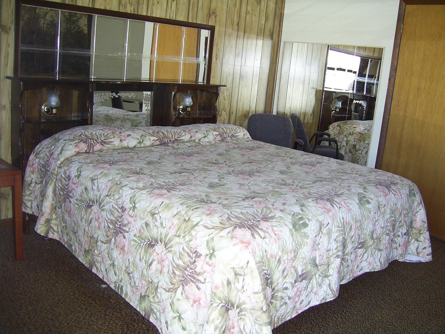 A bedroom with a large bed, a wooden headboard, a mirror, and a chair.