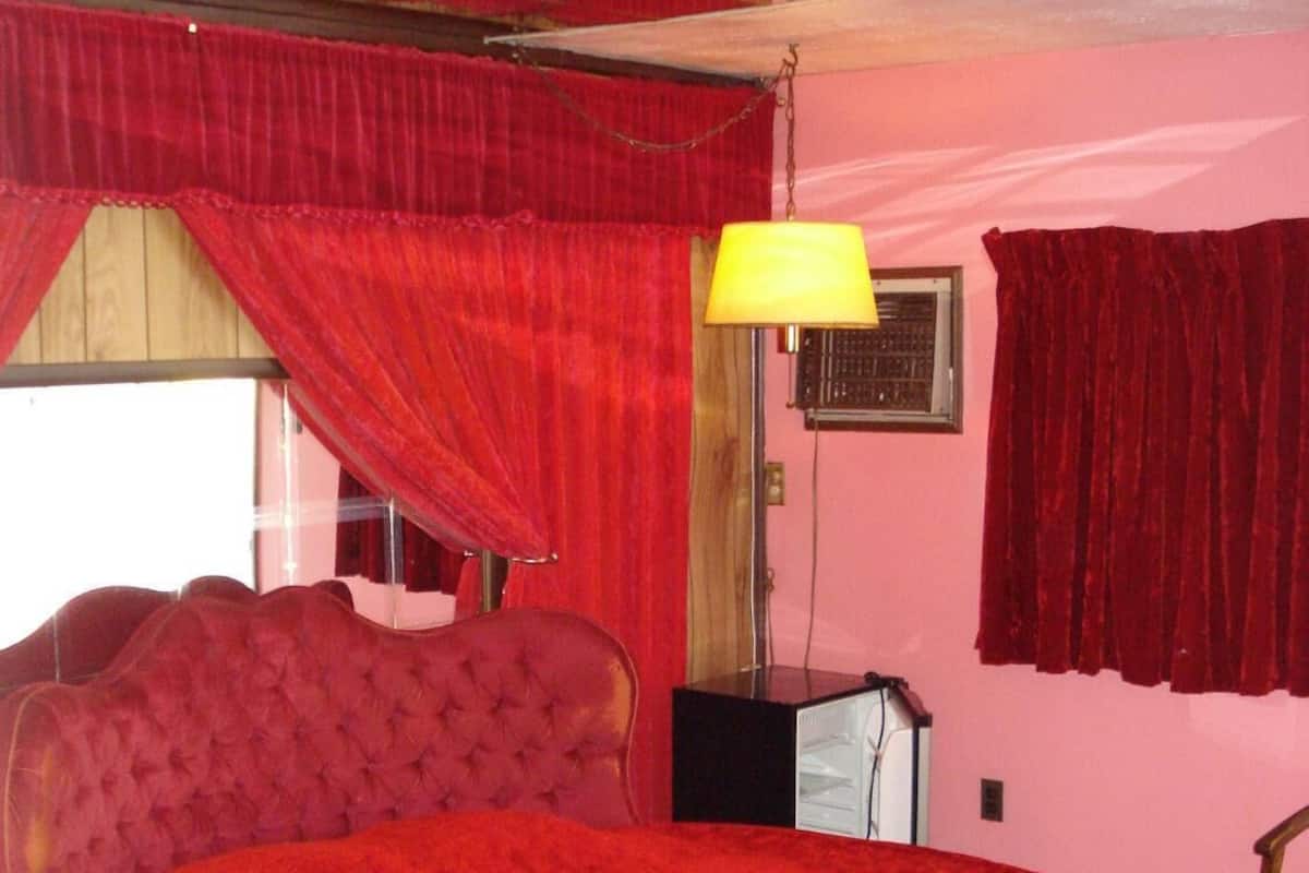 A room with a large round bed, red curtains, a yellow lamp, and a small desk.