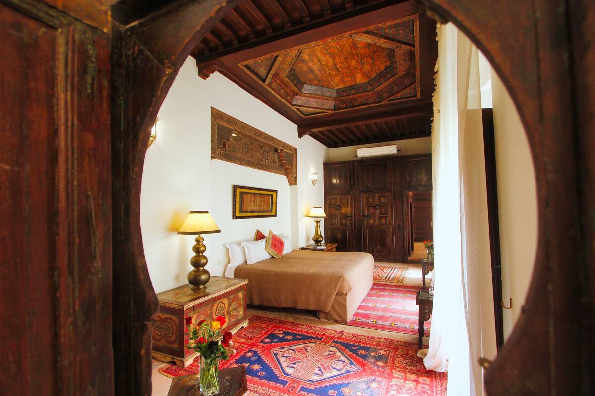 A traditional room with a bed, a nightstand, a lamp, and a carpet.