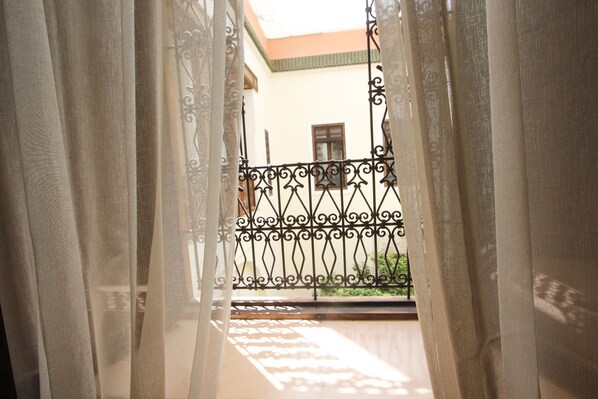 A view through sheer curtains to a balcony with a wrought iron railing, a building with a tiled roof, and a window with a sign. - Riad du Ciel Marrakech (Marrakech)