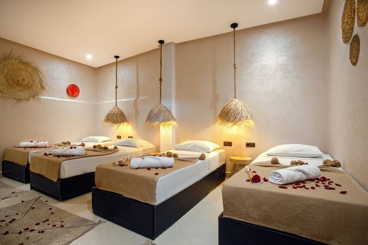 Un cuarto de spa con tres camas, cada una con una toalla y pétalos de rosa.