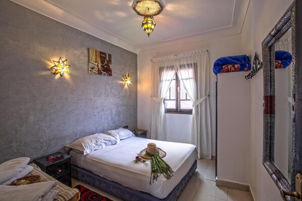 A bedroom with a bed, bedside tables, a window with curtains, a wall-mounted star-shaped light, and a mirror with a decorative frame.