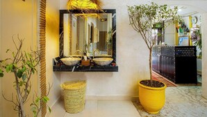 A bathroom with a black marble sink, a mirror, and a hanging light fixture. There is a potted plant and a woven basket on the floor. - Riad Hotel El Kennaria (Marrakech)