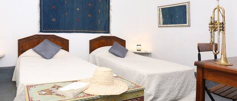 A room with two beds, a wooden table with a brass trumpet, and a decorative box.