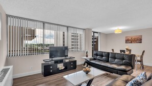 A modern living room with a black leather sofa, a white coffee table, and a TV on a black entertainment unit. - Arlington Fully Furnished Apartments (Arlington)