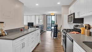 A modern kitchen with white cabinetry, a central island, a built-in oven, and a dining area with a view. - Arlington Fully Furnished Apartments (Arlington)