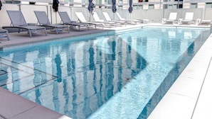 A swimming pool with clear blue water, surrounded by white lounge chairs and umbrellas. - Arlington Fully Furnished Apartments (Arlington)