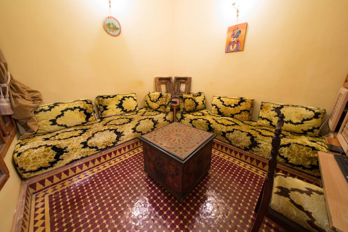 Un salón de estilo marroquí tradicional con sofás estampados, una mesa de centro y suelo de baldosas.