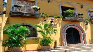 A yellow building with multiple balconies, large potted plants, and a prominent arched entrance. - Hotel Real Granada (Granada)