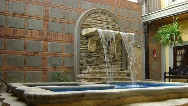 A stone fountain with water cascading into a rectangular pool, set against a brick wall with a stone archway. - Hotel Real Granada (Granada)